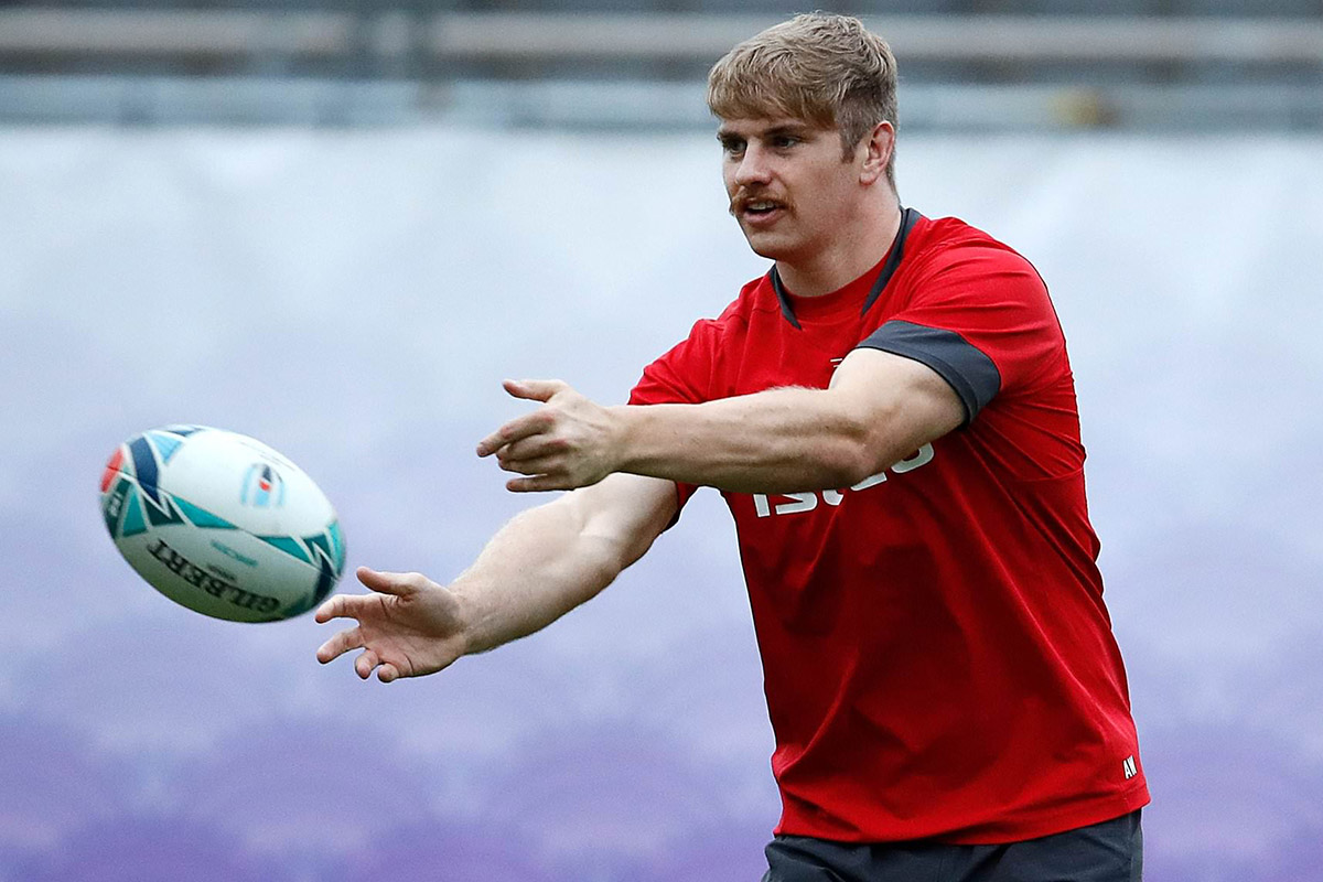 A rugby player wearing a red jersey throwing a rugby ball.